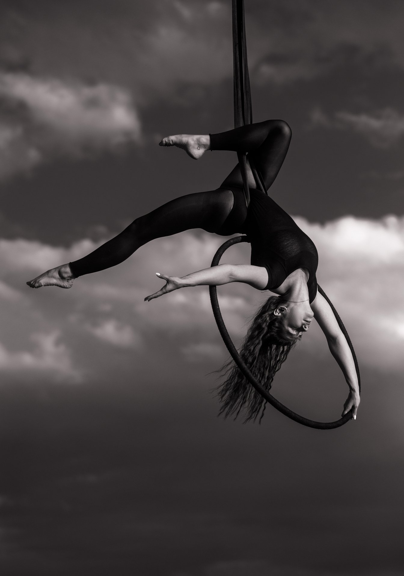 Woman aerialist performs acrobatic elements in hanging aerial hoop.